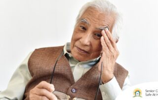 An older adult holds his head and his glasses representing vision problems like macular degeneration.